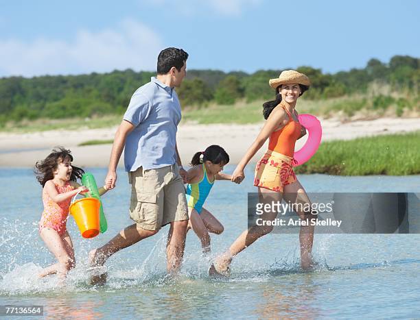 hispanic family walking through water at beach - man and woman holding hands profile stock-fotos und bilder