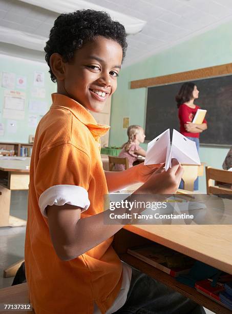 mixed race boy holding paper airplane in class - student sitting in desk side view stock pictures, royalty-free photos & images