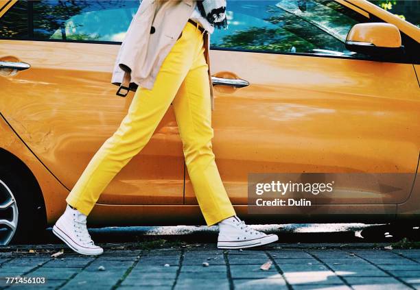 woman in yellow trousers walking past an orange car - parked car stockfoto's en -beelden