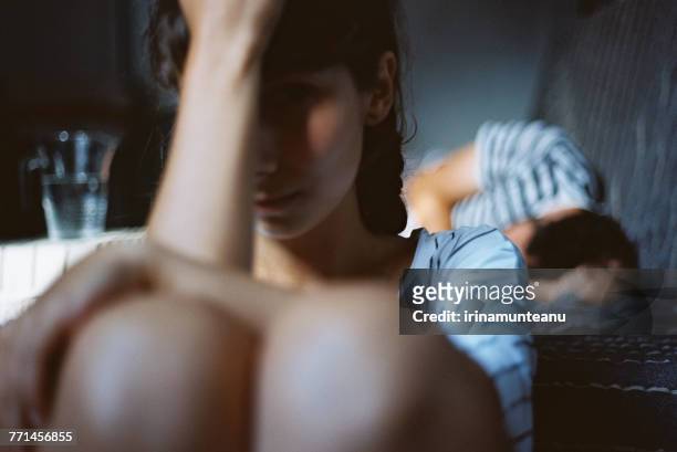 man sleeping in bed with an unhappy woman sitting on the floor next to him - discusión fotografías e imágenes de stock