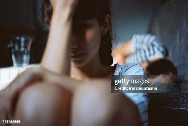 man sleeping in bed with an unhappy woman sitting on the floor next to him - relationship difficulties foto e immagini stock