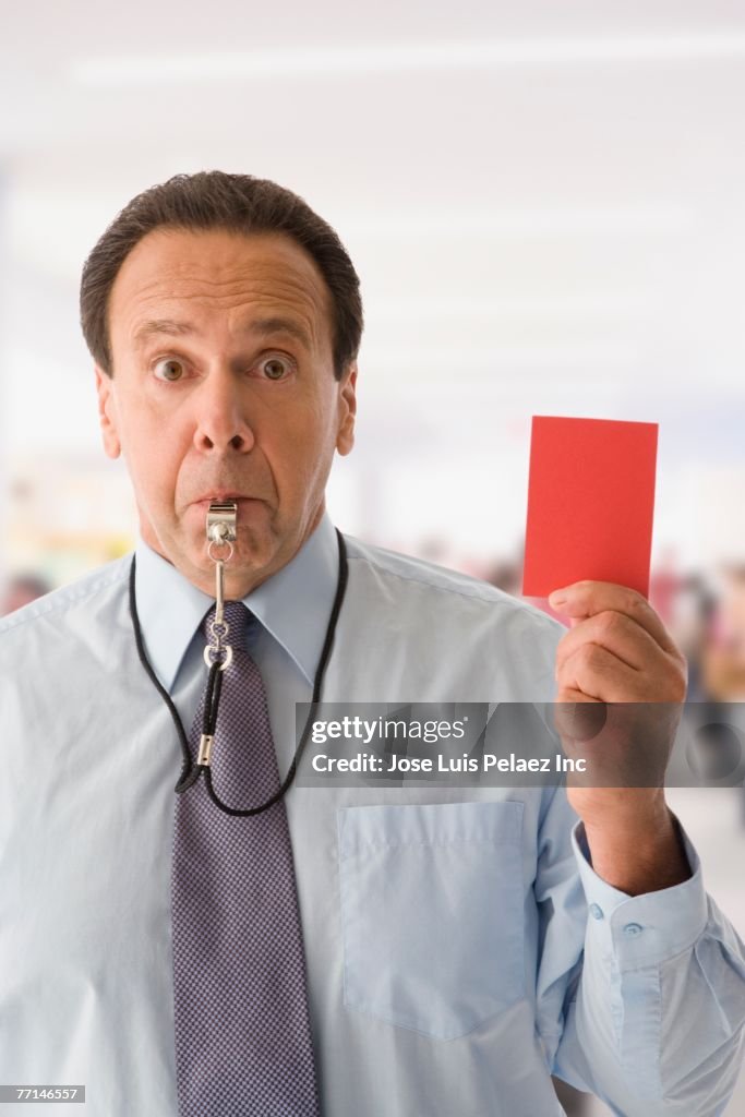 Hispanic businessman holding red card and blowing whistle