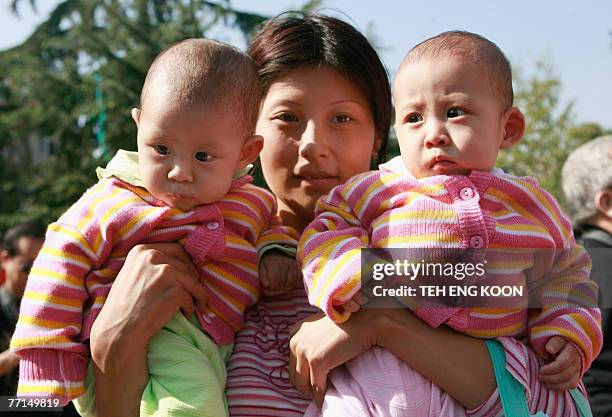 Mother holds her twin baby girls during the Beijing Twins Cultural Carnival at a park in Beijing, 02 October 2007. Chinese officials have been told...