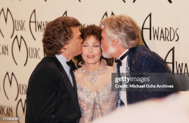 Country singer Loretta Lynn poses for a portrait as Conway Twitty and Kenny Rogers each kiss a cheek at the American Music Awards which were held at...