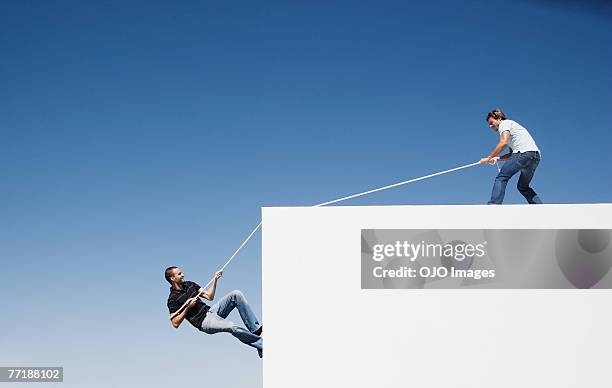 un hombre ayudando a otro hombre suba a una pared - rope fotografías e imágenes de stock