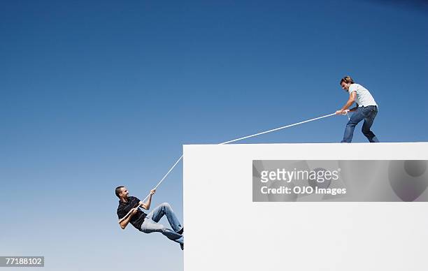 a man helping another man climb up a wall - trust stock pictures, royalty-free photos & images