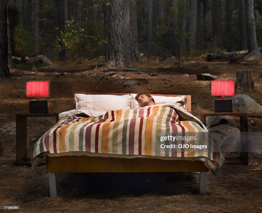 A man sleeping in a bed outdoors in the woods