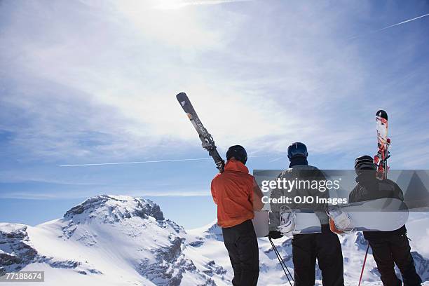 skiers and a snowboarder on a mountain carrying their equipment - skiing and snowboarding stockfoto's en -beelden