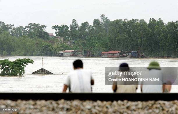 Men sit on a dike watching the flooded Ma river in the central province of Thanh Hoa, 05 October 2007, after Typhoon Lekima hit the central part of...