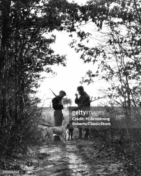 1920s 1930s TWO MEN HUNTERS ANONYMOUS SILHOUETTED WITH DOGS ON COUNTRY LANE