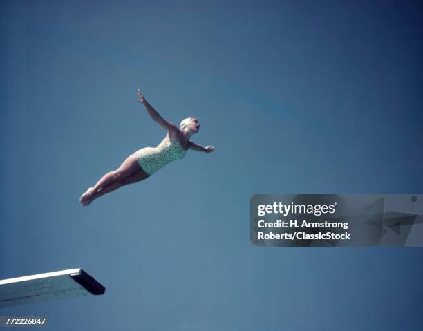 1950s WOMAN WEARING WHITE ONE PIECE BATHING SUIT AND CAP SWAN DIVING OFF HIGH BOARD AGAINST BLUE SKY