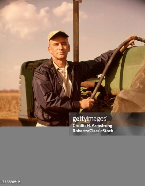 1960s PORTRAIT OF SERIOUS MAN FARMER LOOKING AT CAMERA FUEL INTO TRACTOR