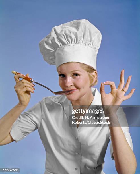 1960S WOMAN CHEF WEARING TOQUE LOOKING AT CAMERA TASTING FOOD MAKING OKAY SIGN SMILING