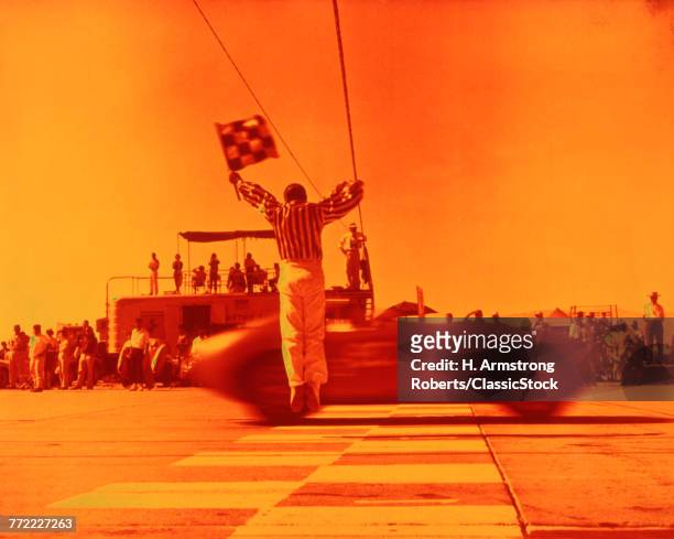 1970s MAN WAVING CHECKERED FLAG AT FINISH LINE END OF SPORTS CAR RACE ORANGE FILTER
