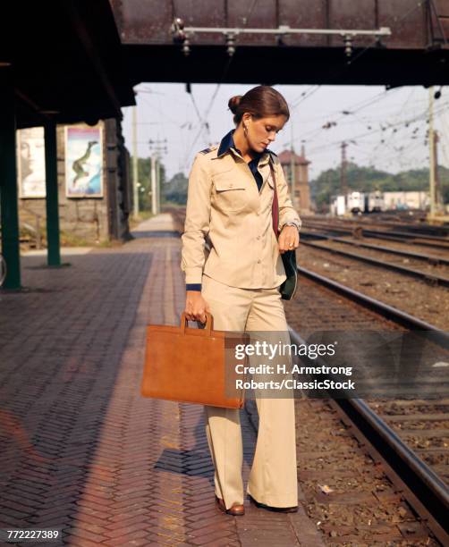 1970s YOUNG BUSINESSWOMAN ON TRAIN PLATFORM LOOKING AT WATCH BRIEFCASE COMMUTER