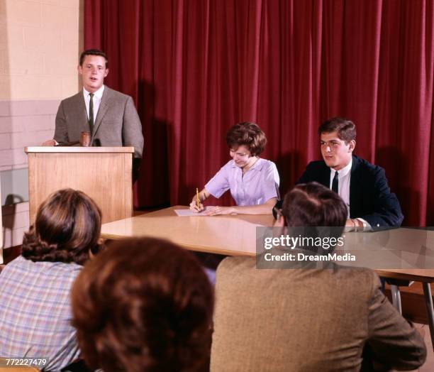 1960s MALE STUDENT AT PODIUM PANEL CLASS DEBATE PUBLIC SPEAKING STUDENT GOVERNMENT STUDY EDUCATION