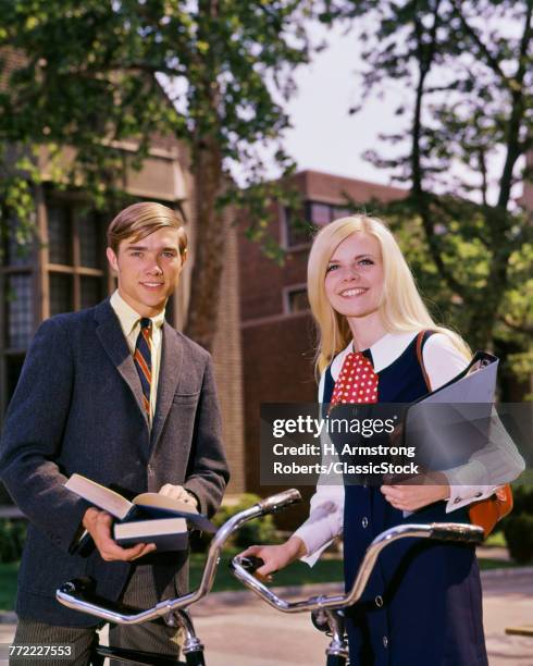 1960s PORTRAIT STUDENT COUPLE ON CAMPUS WITH BIKES AND BOOKS LOOKING AT CAMERA