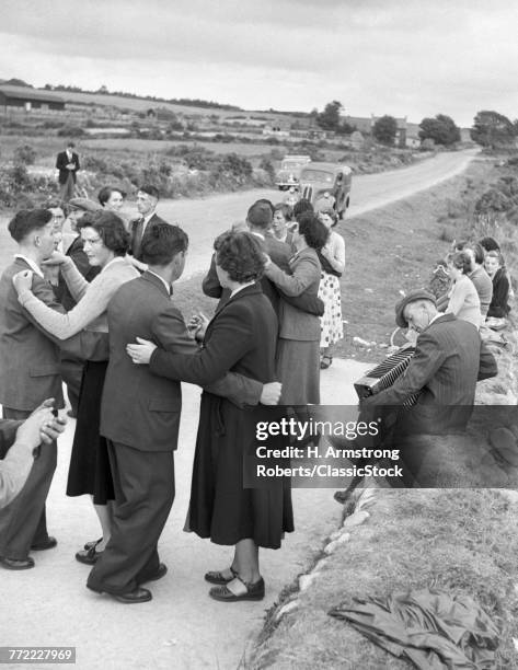 1950s GROUP OF MEN AND WOMEN DANCING OUTDOOR IN A RURAL ROAD NEAR BANTRY IRELAND