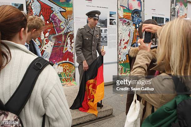 Tourists take pictures of an actor posing in a uniform of the former East German border police and carrying an East German flag at a memorial to the...