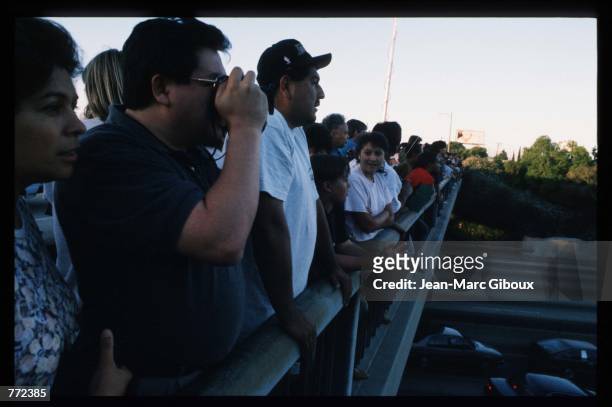 People watch and wave from a freeway overpass as police cars pursue a Ford Bronco driven by Al Cowlings, carrying fugitive murder suspect O.J....