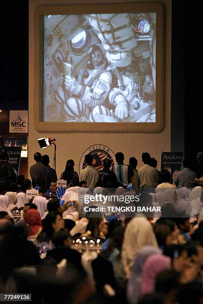 Invited guests and school children watch a giant monitor as Malaysia's first astronaut Sheikh Muszaphar Shukor is seen on-screen as he reaches orbit...