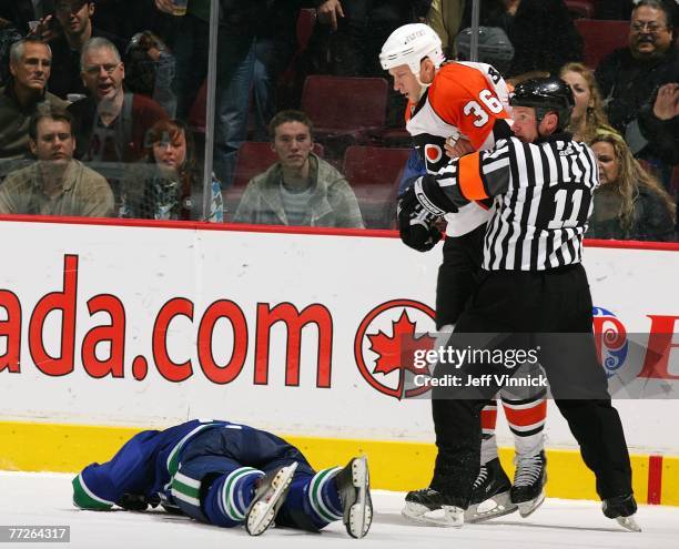 Ryan Kesler of the Vancouver Canucks lays motionless on the ice as Jesse Boulerice of the Philadelphia Flyers is held back by referee Kelly...