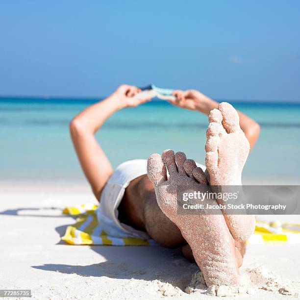 bare feeet of man lying on beach with book - livre broché photos et images de collection