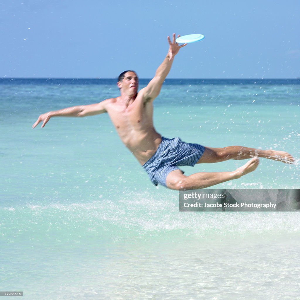 Man jumping to catch flying disc on beach
