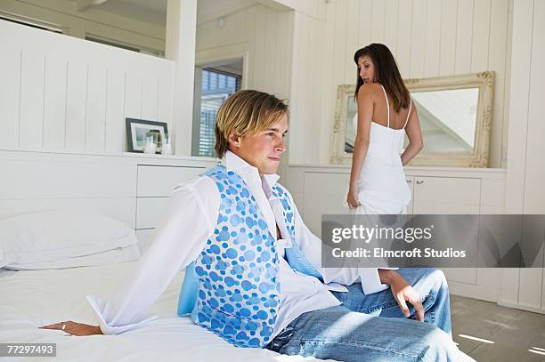 woman glancing at young man sitting on bed - spogliarsi foto e immagini stock