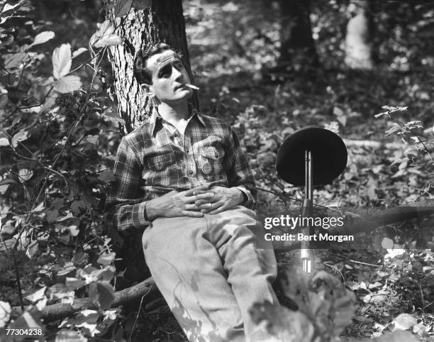 An unidentified hunter leans back against a tree and smokes a cigarette, his hat balanced on the barrel of his rifle beside him ,New York, mid to...