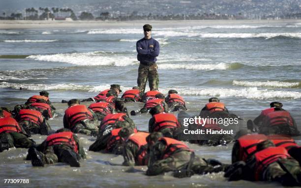 During a Hell Week surf drill evolution, a Navy SEAL instructor assists students from Basic Underwater Demolition/SEAL class 245 with learning the...
