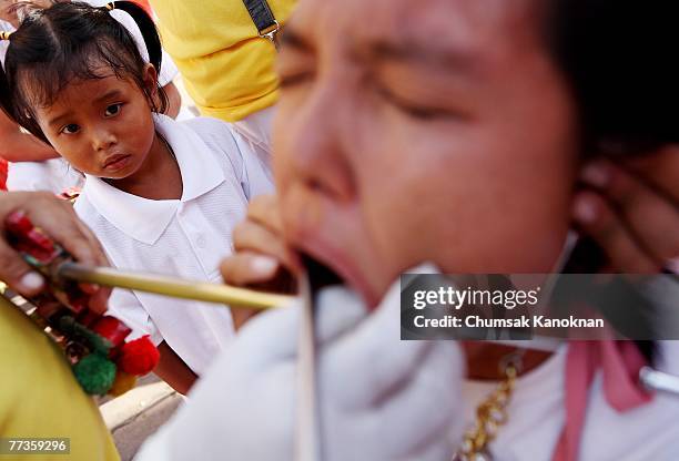 Girl look at devotee of the Chinese shrine of Jui Tui pierces her cheek with metal spike during a procession of Vegetarian Festival on October 17 in...