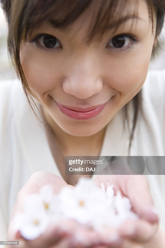 Portrait of a woman scooping up cherry flowers with hands, smiling and looking at camera, front view, close up, differential focus, Japan