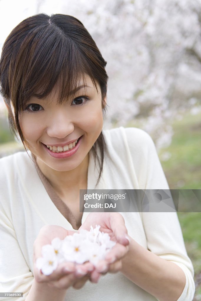 Portrait of a woman scooping up cherry flowers with hands, smiling and looking at camera, front view, Japan