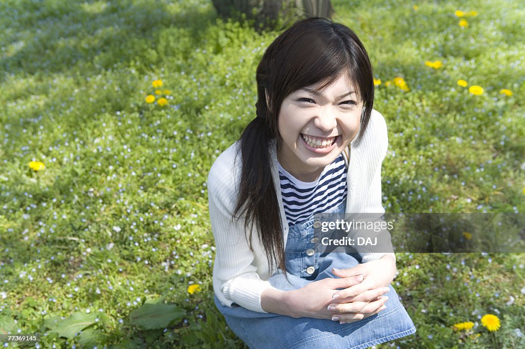 Portrait of a woman crouching down and looking at camera on field, high angle view, Japan