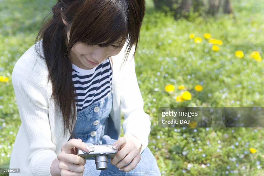 Woman smiling and holding a digital camera on lawn, front view, Japan