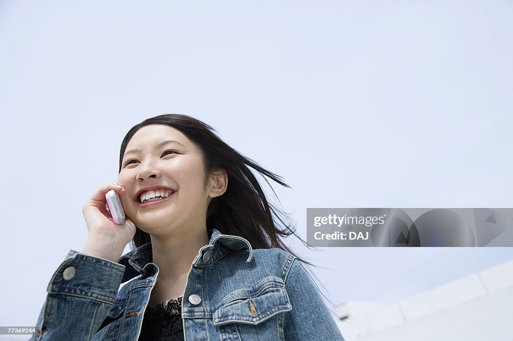 Woman using mobile phone under the blue sky, low angle view, blue background, Japan