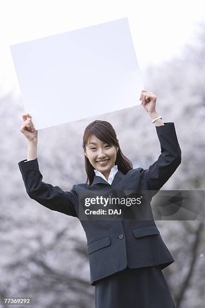 businesswoman lifting a white board, three quarter length, front view - three quarter front view stockfoto's en -beelden