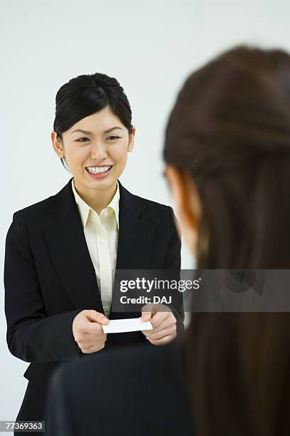 businesswoman exchanging business cards, smiling, three quarter length, front view, rear view - three quarter front view stockfoto's en -beelden