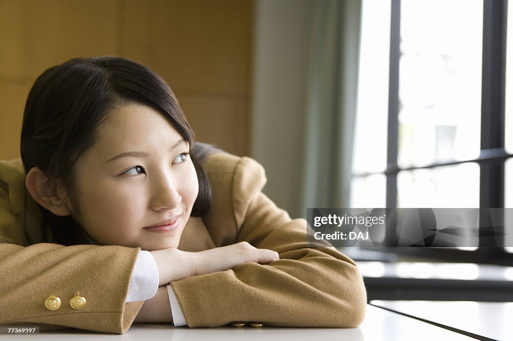 Teenage girl sitting and leaning on desk in classroom, smiling and looking away