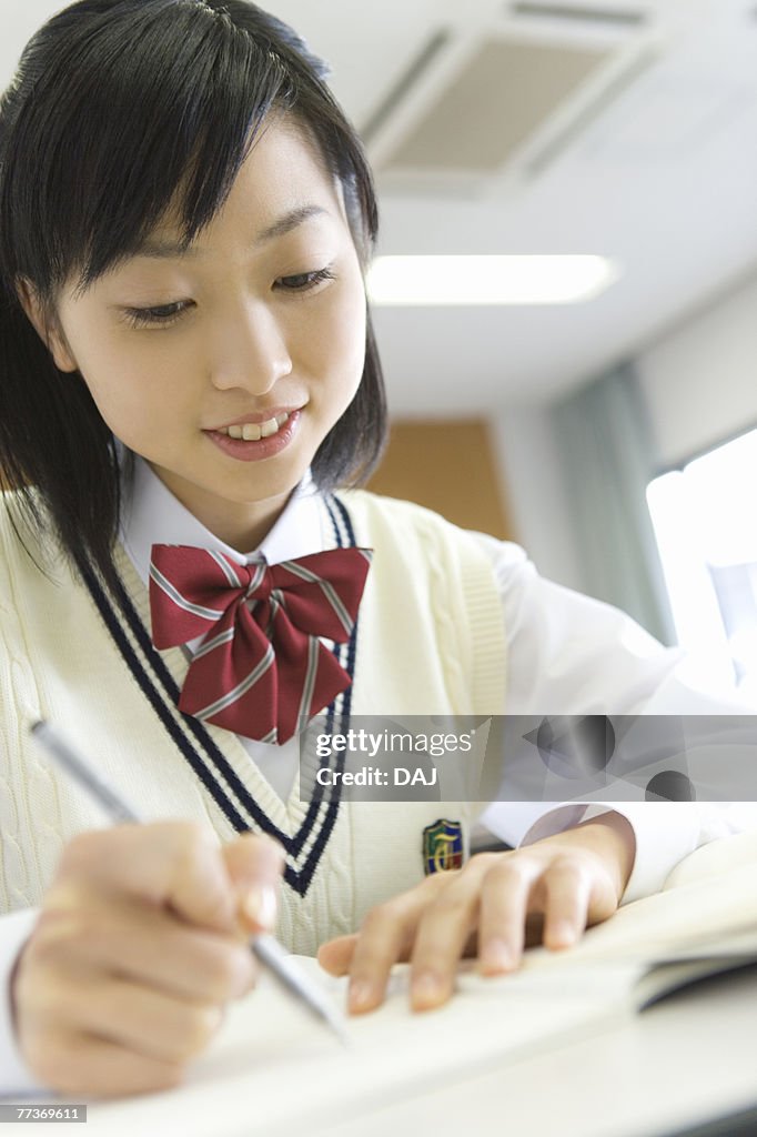 Teenage girl studying at desk in classroom, smiling