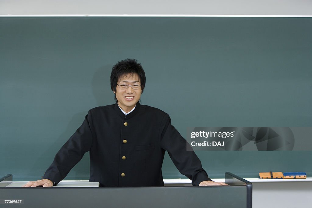Portrait of a teenage boy standing in front of blackboard, smiling and looking at camera