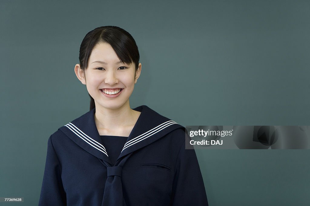 Portrait of a teenage girl standing in front of blackboard, smiling and looking at camera, green background