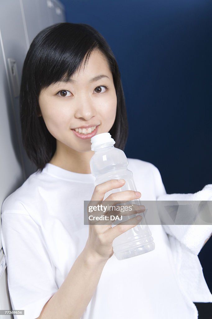 Portrait of a teenage girl in gym cloth smiling and holding a bottle of water in locker room