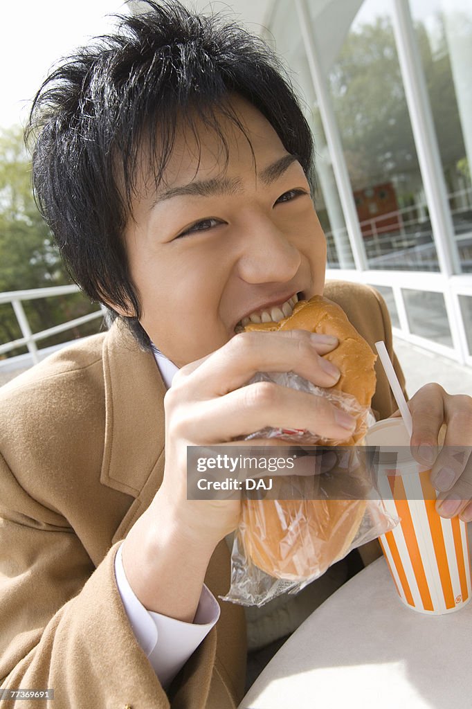 Teenage boy eating bread and holding disposable cup at terrace