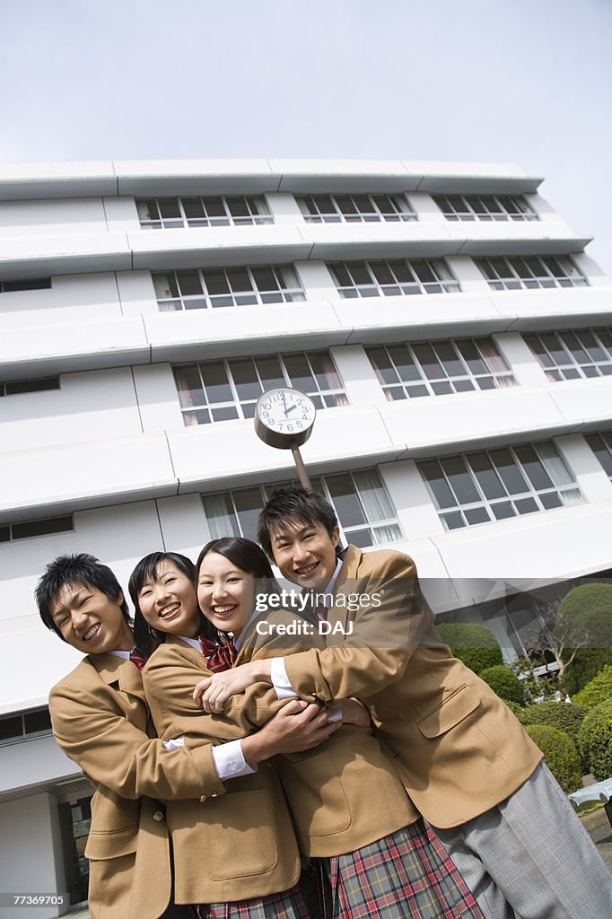 Portrait of four high school students embracing each other, smiling and looking at camera