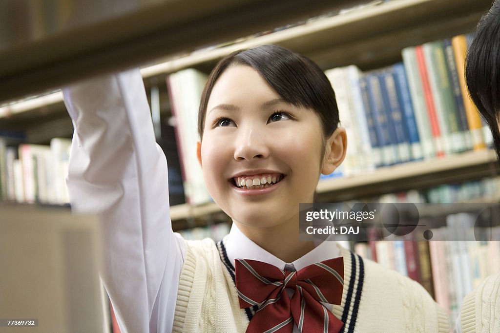 Teenage girls smiling and standing between bookcases