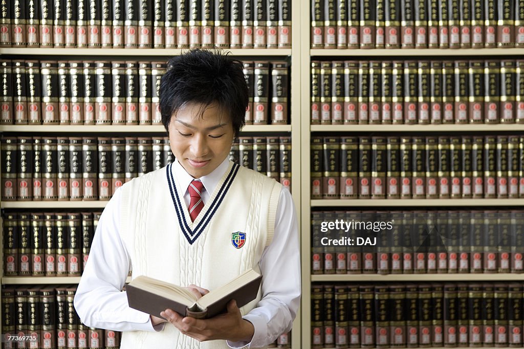 Teenage boy reading a book in front of bookcase