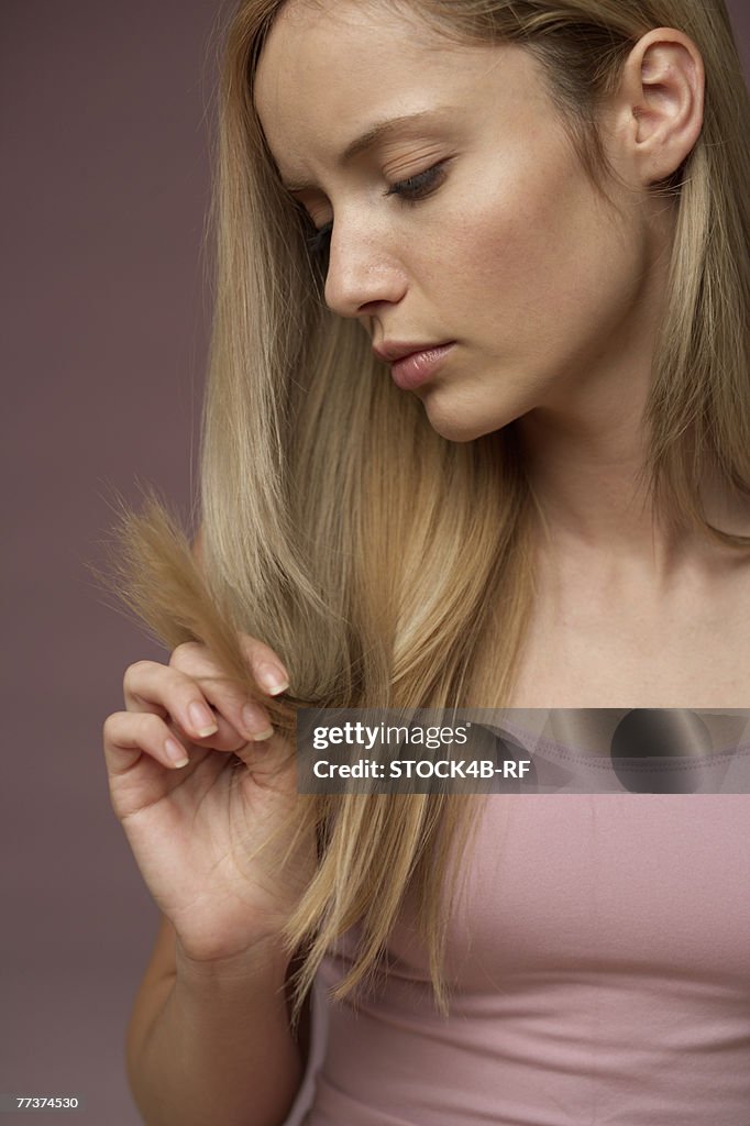 Young blonde woman unhappy about split ends of her blonde long hair