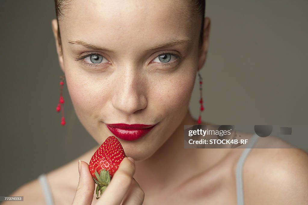 Young woman with a red strawberry under her red lips (part of), close-up